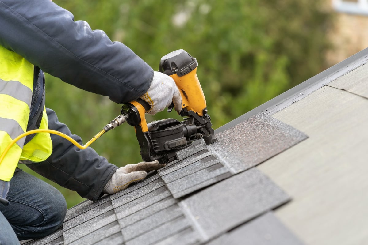 Unrecognizable roofer worker installing asphalt tile on top of the roof