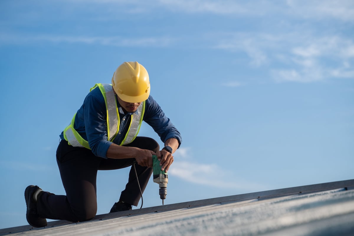 Worker repairing roof on construction site using electric drill