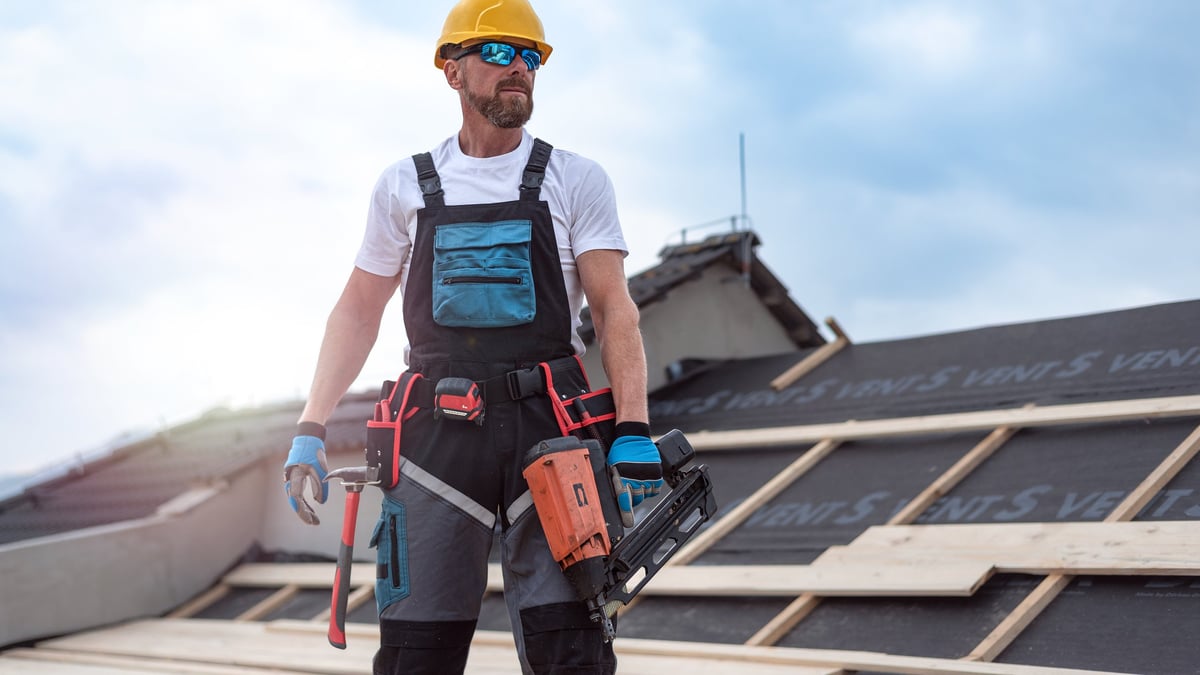 Carpenter nailing timber board on roof using electric nailer