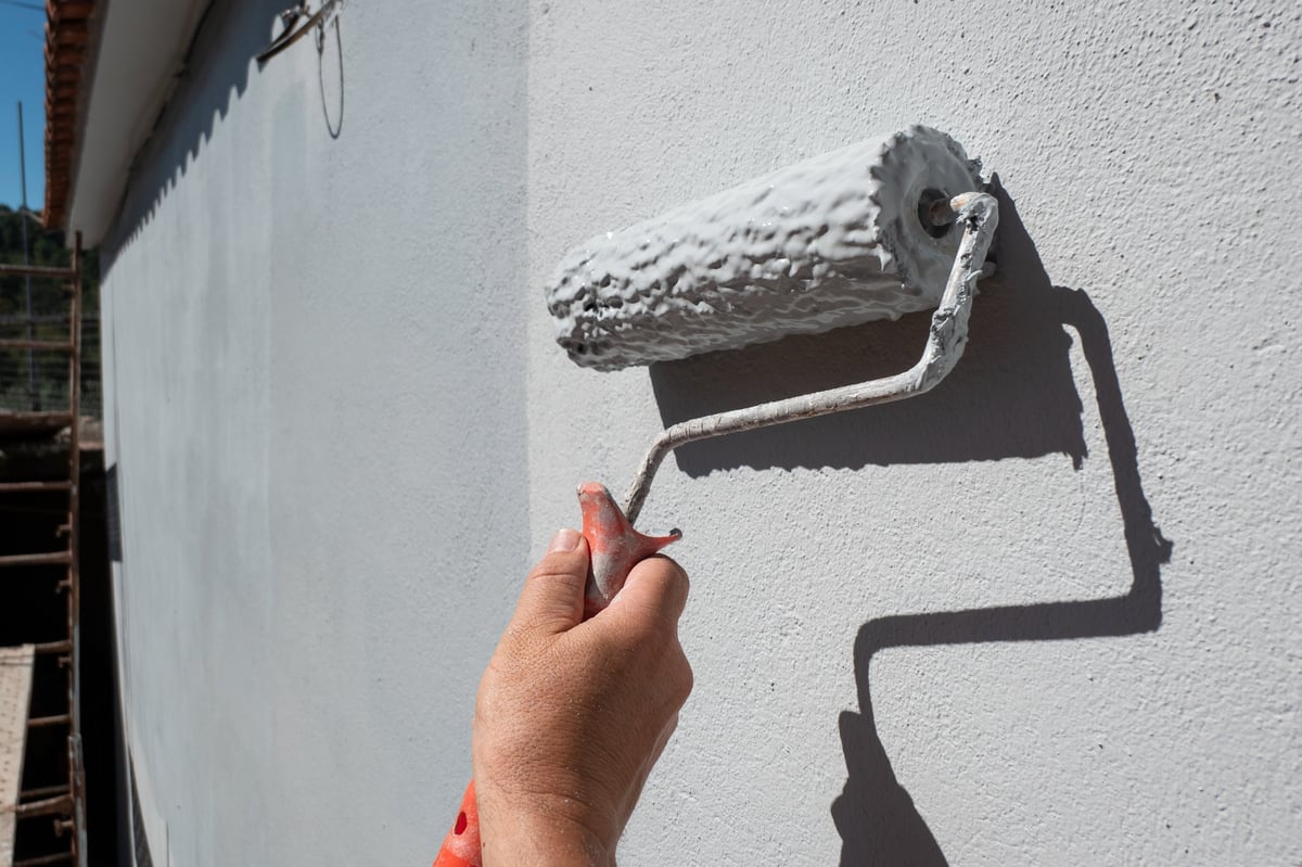 Painter's hand holding roller filled with paint for exterior wall