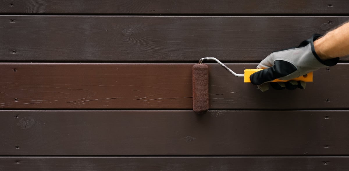 Hand with paint roller painting wooden house exterior