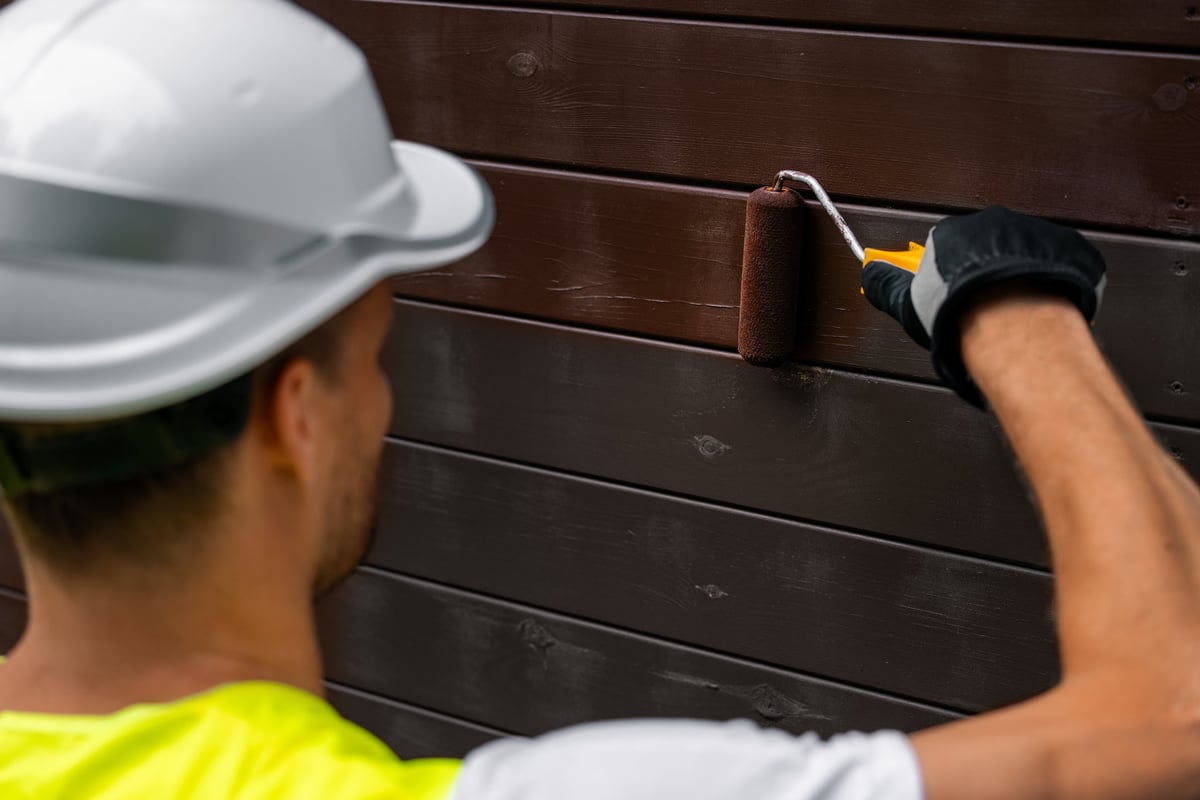 Man with paint roller painting wooden house facade