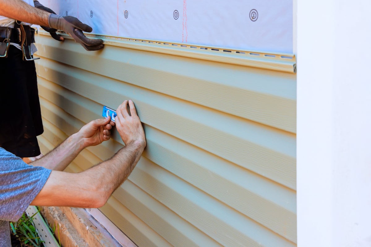 Workers measuring and installing vinyl siding on house exterior