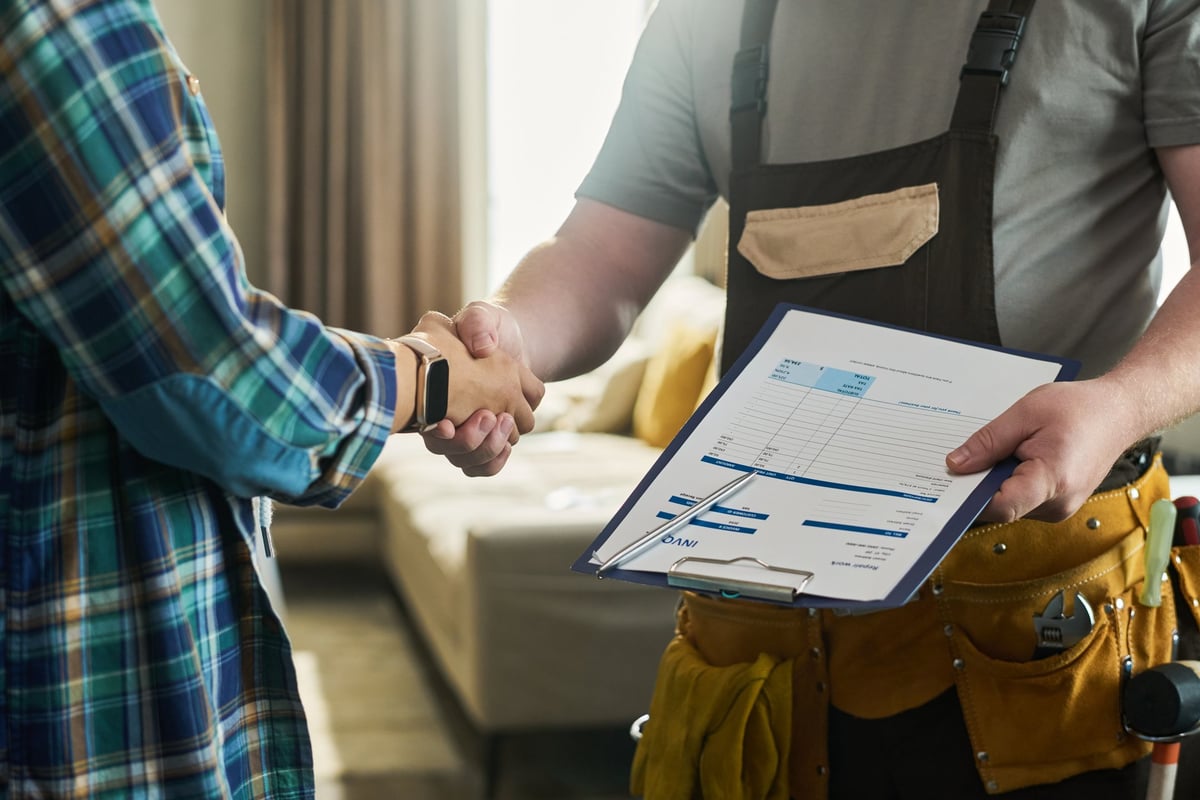 Middle aged man holding invoice clipboard shaking hands with homeowner