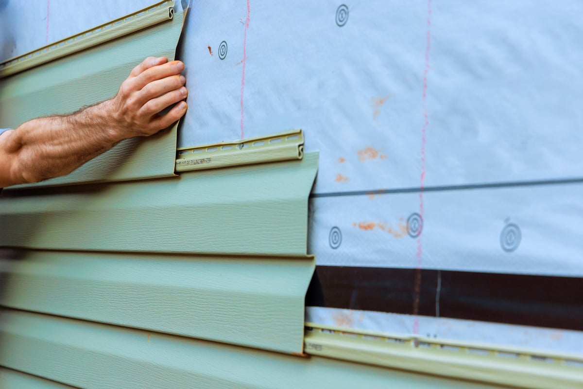 Construction worker fitting section of green PVC siding onto wall