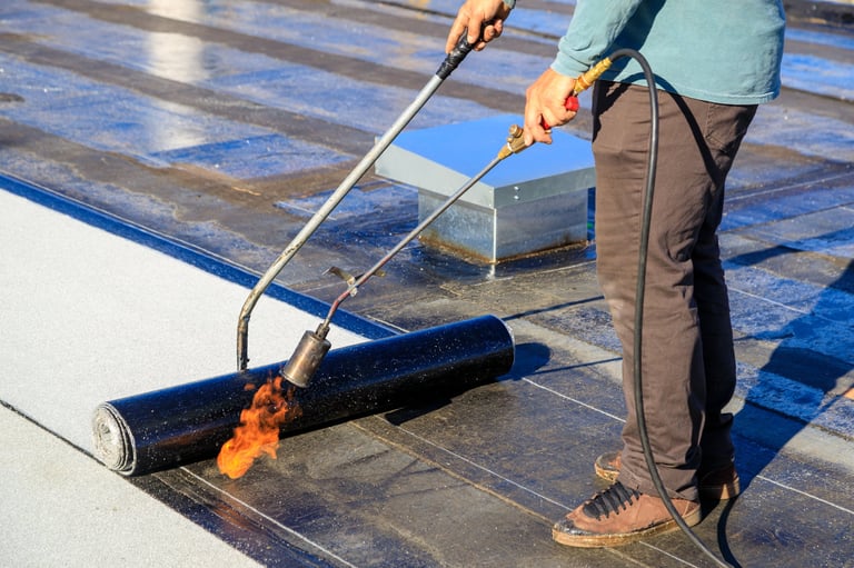 Roofer torching membrane on flat roof