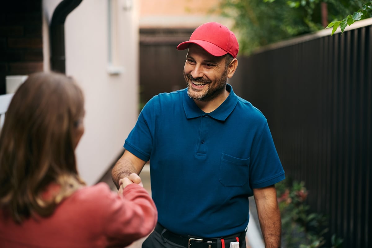 Happy handyman handshaking with customer in backyard