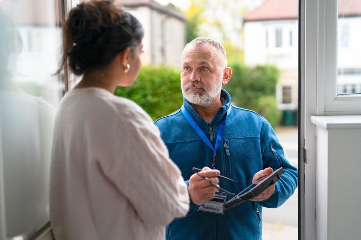 Man in blue jacket engaging with woman holding clipboard at doorway